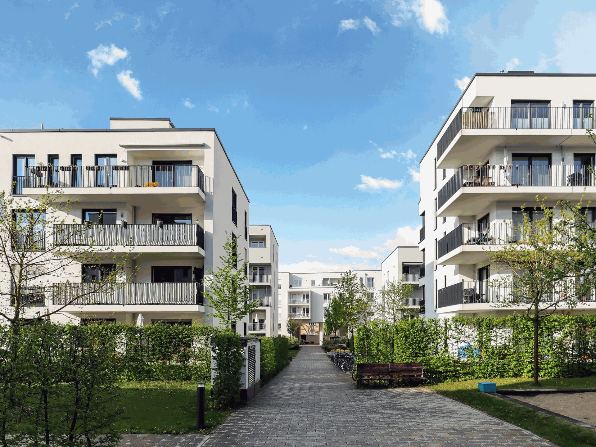 Contemporary white apartment buildings with balconies along a landscaped path